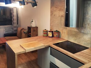 A modern kitchen with a wooden countertop, an induction cooktop, and a built-in oven. There are three spice containers on the counter. - Bolquère Ski Slopes Apartment (Bolquere)
