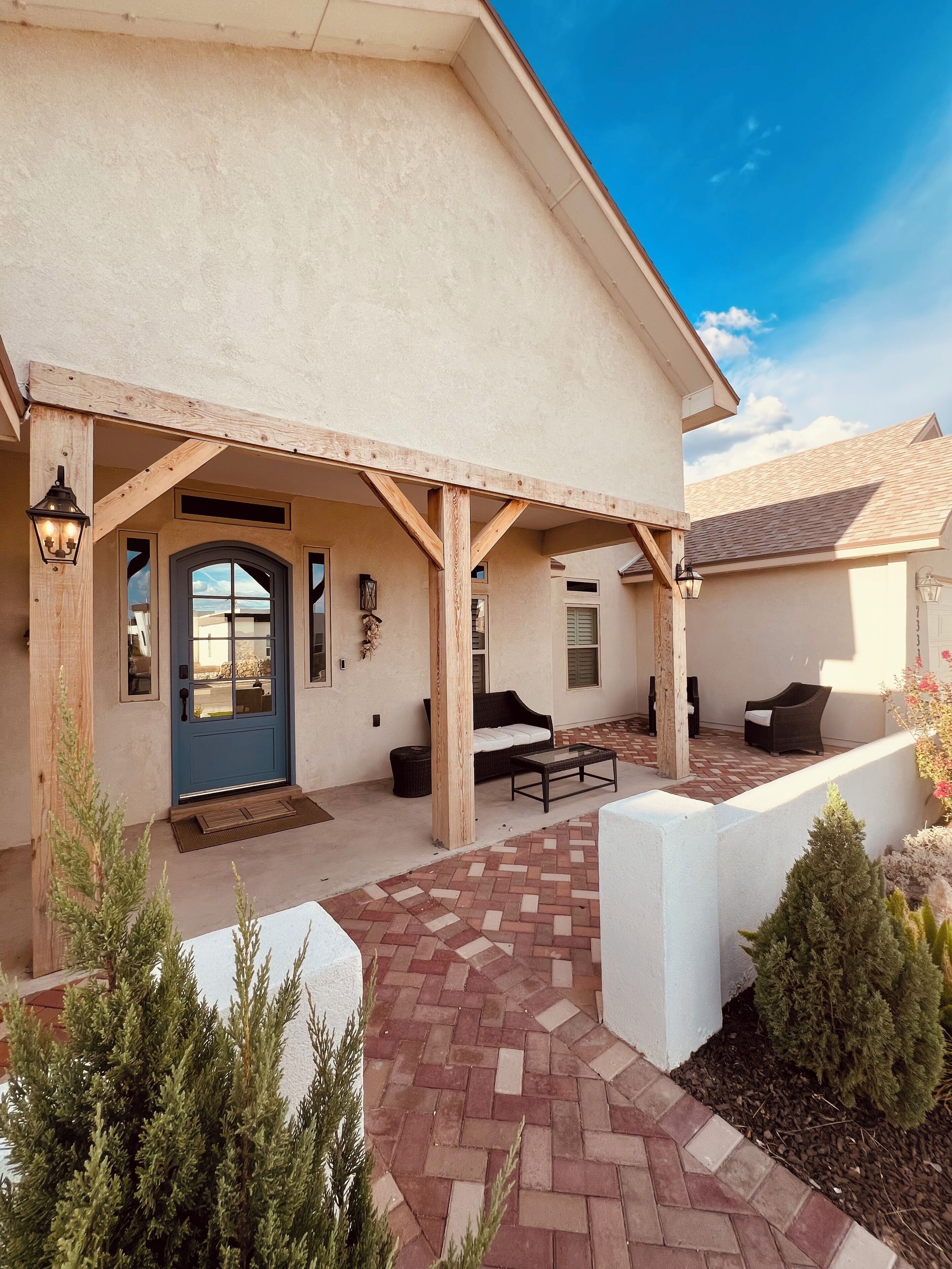 A covered patio with a brick floor, outdoor seating, and a blue door.