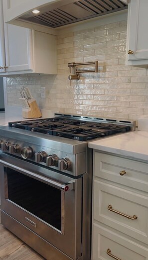 A kitchen with a stainless steel stove, white cabinets, and a tiled backsplash.