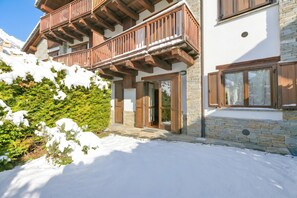 Una xalet de dos pisos amb balcons de fusta, parets de pedra i entrada coberta de neu.