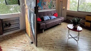 A room with a sofa, a painting, a plant, and a window. - Industrial DesignTerrace El Poblado fast WIFI (Medellín)