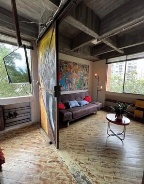 Ein Zimmer mit einer Couch, einem Bild, einer Pflanze und einem Fenster.