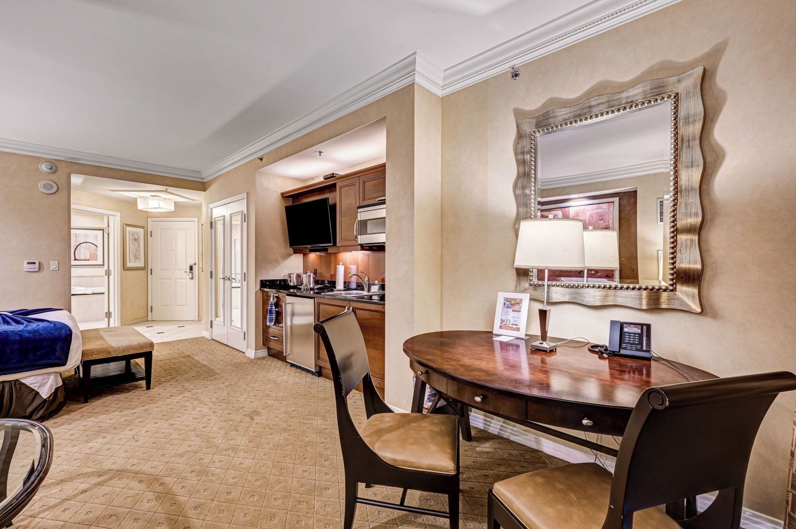 A hotel room with a dining area, a kitchen, and a large mirror.