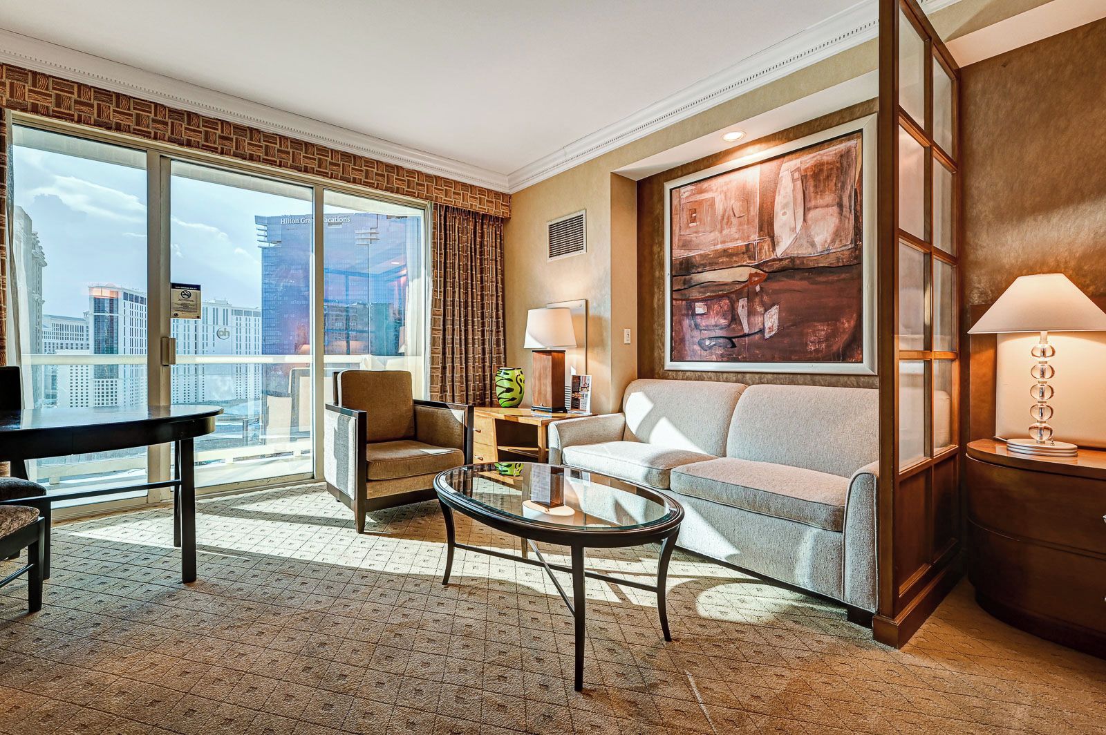 Une chambre d’hôtel moderne dotée d’une grande fenêtre, d’un canapé, d’un fauteuil, d’une table basse et d’une lampe.