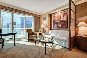 Una habitación de hotel moderna con un ventanal grande, un sofá, una silla, una mesita de centro y una lámpara.