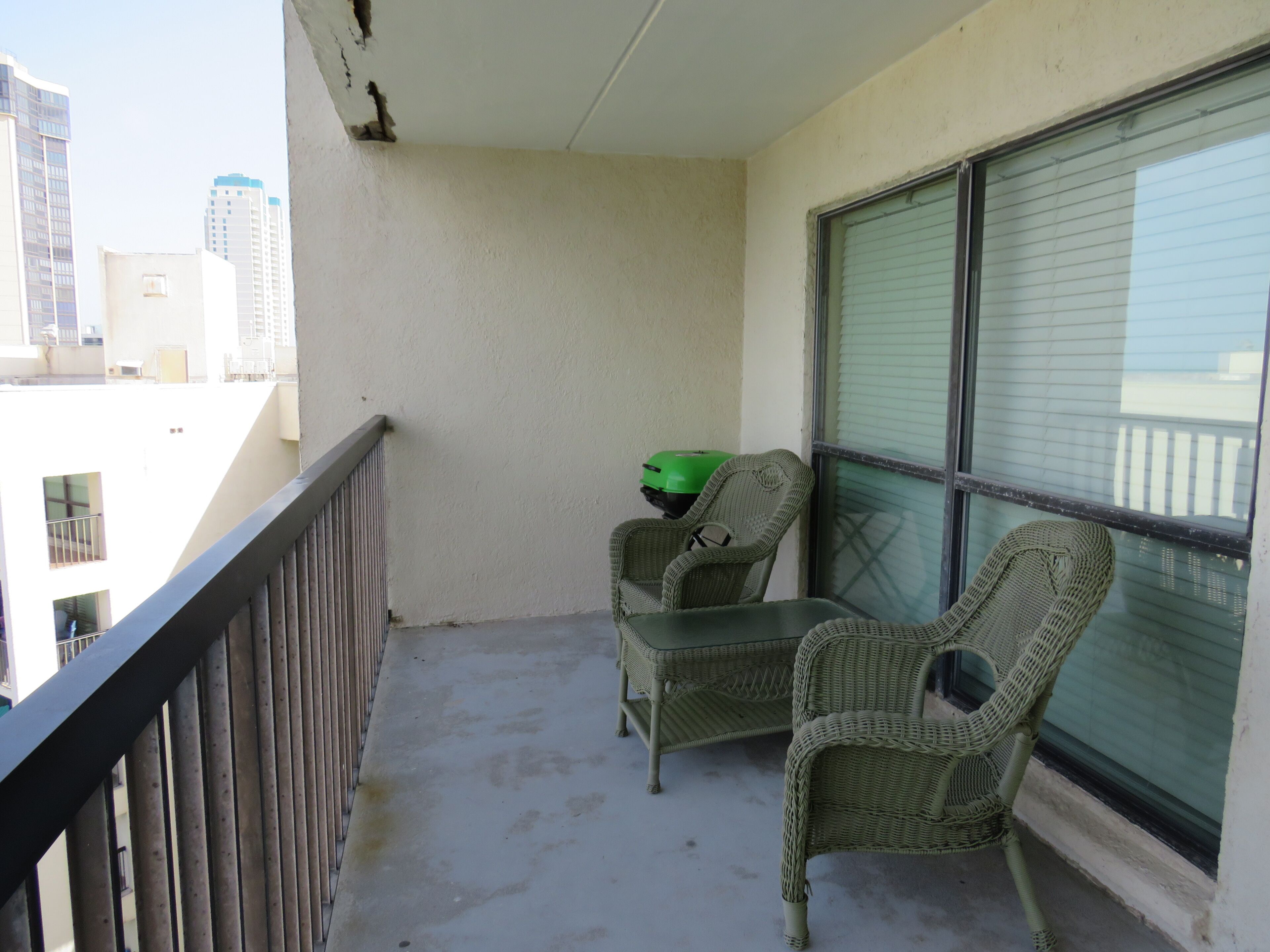Ein Balkon mit zwei Korbstühlen, einem Tisch, einem grünen Topf und Blick auf Gebäude.