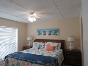 A bedroom with a bed, two bedside tables with lamps, a ceiling fan, and a beach-themed painting on the wall. - SPI Waterfront Getaway - Wake up to Ocean Views (South Padre Island)