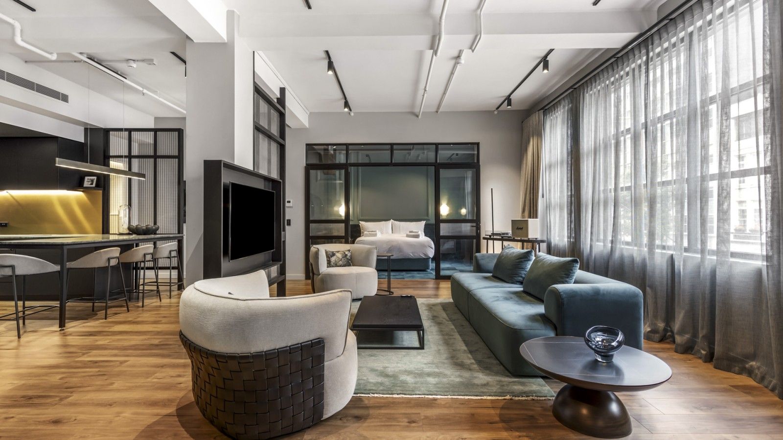 A modern hotel room with a living area, a sofa set, a dining table with chairs, a flat-screen TV, and a large window with curtains.