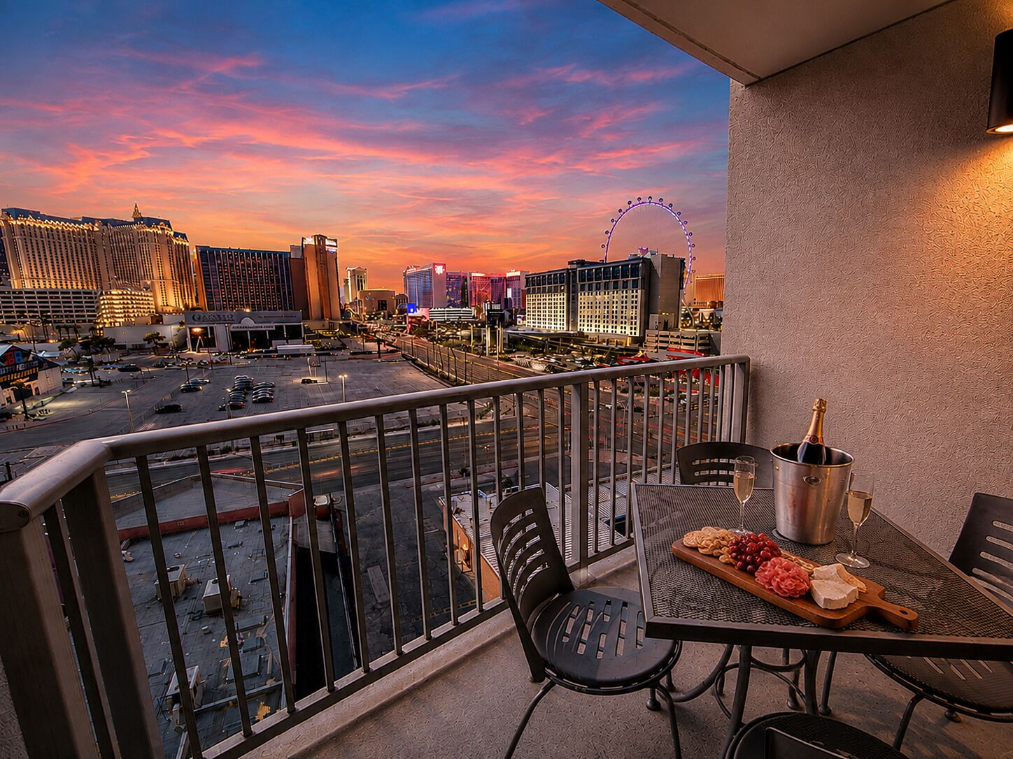 A balcony with a table set for a meal, a bottle of champagne, and a view of a cityscape with a Ferris wheel.