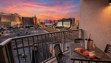 A balcony with a table set for a meal, a bottle of champagne, and a view of a cityscape with a Ferris wheel.