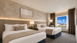 Habitación de hotel con dos camas, un ventanal amplio con vistas a la ciudad y un diseño moderno.
