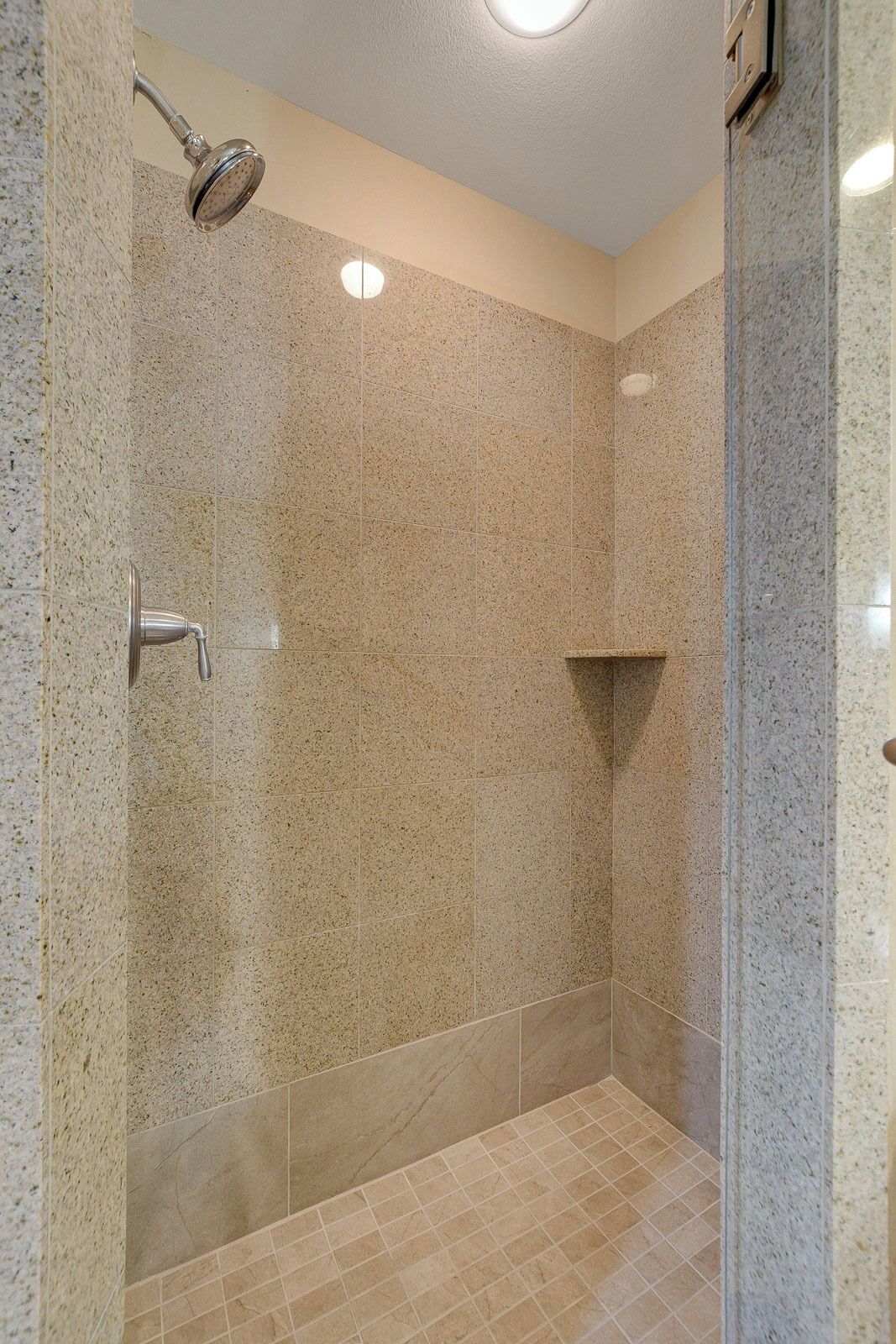 A shower area with a handheld showerhead, a wall-mounted faucet, and a tiled floor.