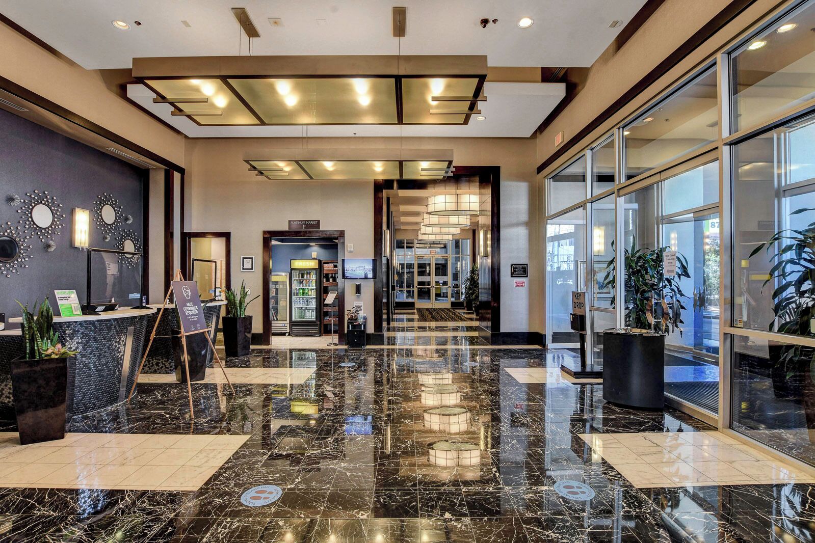 A hotel lobby with a marble floor, reception desk, and a glass door leading to the entrance.