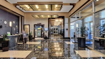 A hotel lobby with a marble floor, reception desk, and a glass door leading to the entrance.