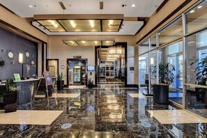 A hotel lobby with a marble floor, reception desk, and a glass door leading to the entrance.