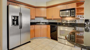 Una cocina con electrodomésticos de acero inoxidable, gabinetes de madera y piso de baldosas.