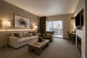 A modern hotel room with a sofa, armchair, coffee table, and a flat-screen TV mounted on the wall.