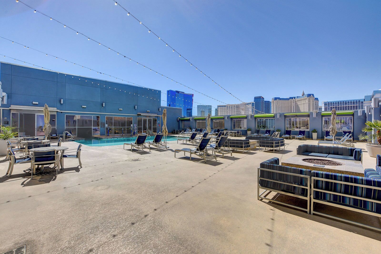 A rooftop pool area with lounge chairs and umbrellas, surrounded by city buildings.