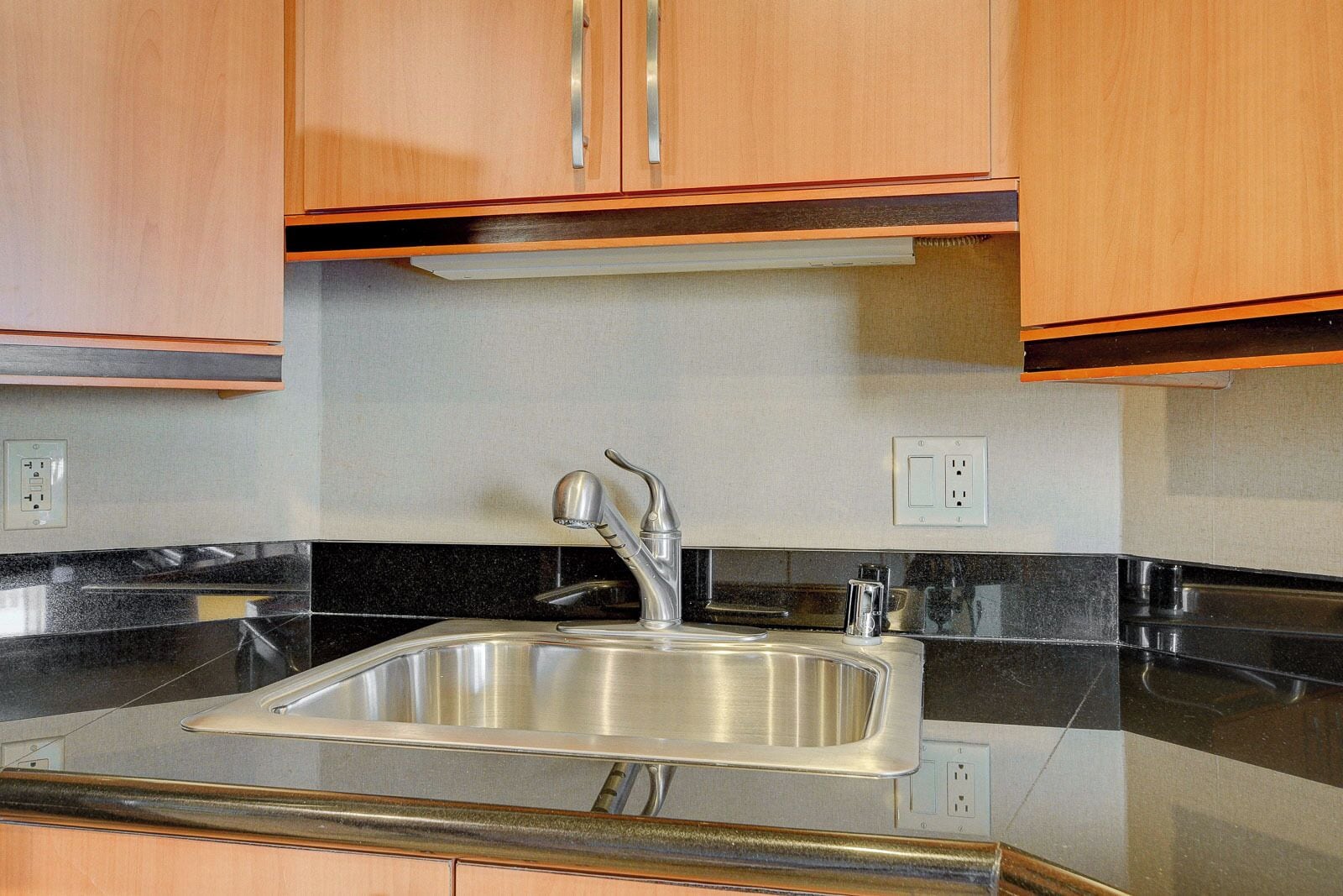 Cocina con pileta de acero inoxidable, muebles de madera y encimeras negras.