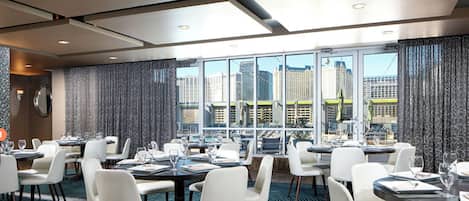 Un espace de restauration d’hôtel avec des tables dressées pour les clients, de grandes fenêtres offrant une vue sur la ville et un design de plafond moderne.