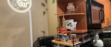 Cozinha com barra de café, máquina de café, micro-ondas e diversos utensílios para café.