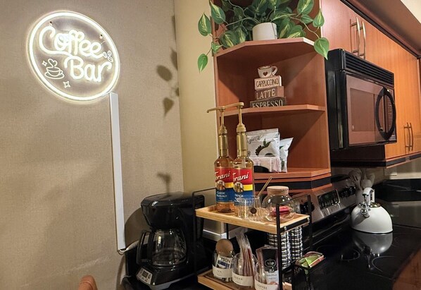 A kitchen with a coffee bar sign, a coffee maker, a microwave, and various coffee-related items.