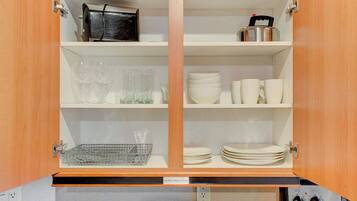 A kitchen cabinet with shelves containing glassware, plates, and a kettle.