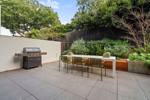 Eine Terrassenanlage im Freien mit Grill, Tisch und Stühlen.
