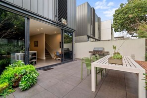 Un patio exterior moderno con una mesa de comedor, sillas y una parrilla.