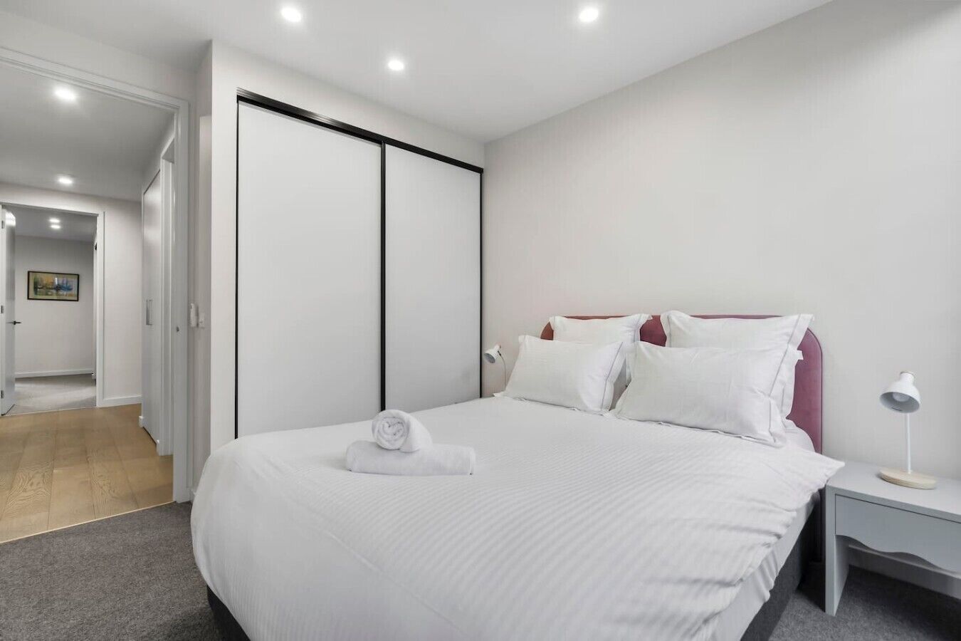A hotel room with a bed, a nightstand, a lamp, and a door leading to another room.