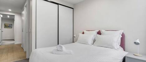 A hotel room with a bed, a nightstand, a lamp, and a door leading to another room.
