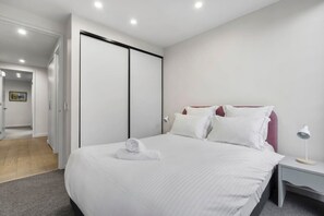 Une chambre d’hôtel avec un lit, une table de chevet, une lampe et une porte donnant sur une autre pièce.