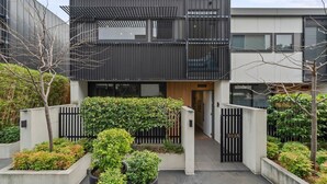 A modern two-story residential building with a gated entrance, a small covered walkway, and a variety of potted plants. - Leafy Caulfield Townhouse - (pool, car park, BBQ) (Caulfield North)