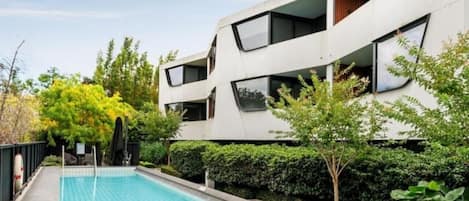 A modern building with a swimming pool, surrounded by greenery and trees.
