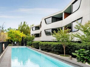 Un edificio moderno con piscina, rodeado de vegetación y árboles.