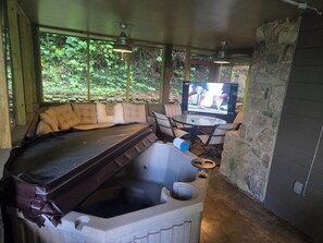 A room with a stone wall, a hot tub, a sofa, a TV, and a table. - Mountain Memories Gatlinburg Home Sleeps 9 NO Winding Roads (Gatlinburg)