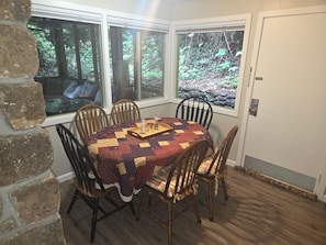 A dining room with a round table, six wooden chairs, and a quilted tablecloth. - Mountain Memories Gatlinburg Home Sleeps 9 NO Winding Roads (Gatlinburg)