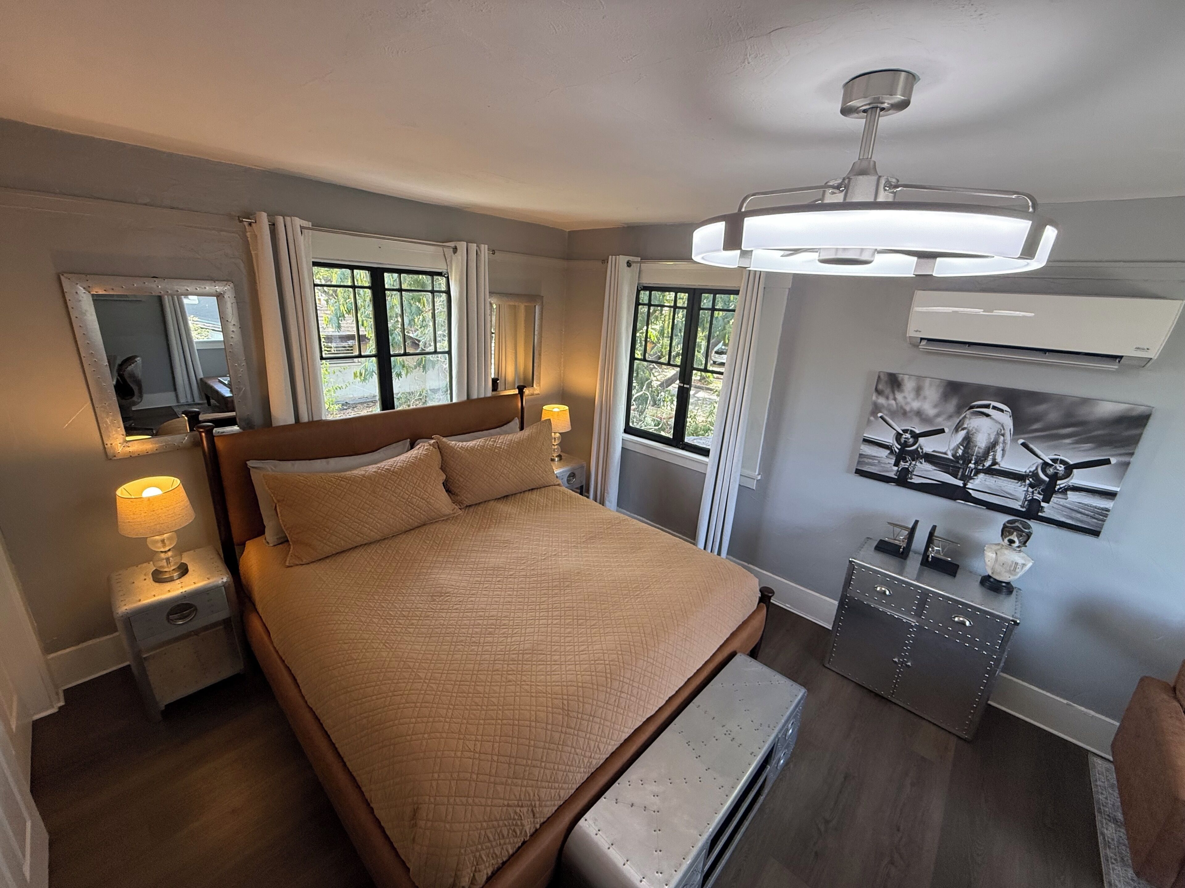 Quarto com cama, abajures, cômoda, espelho e janela com cortinas.