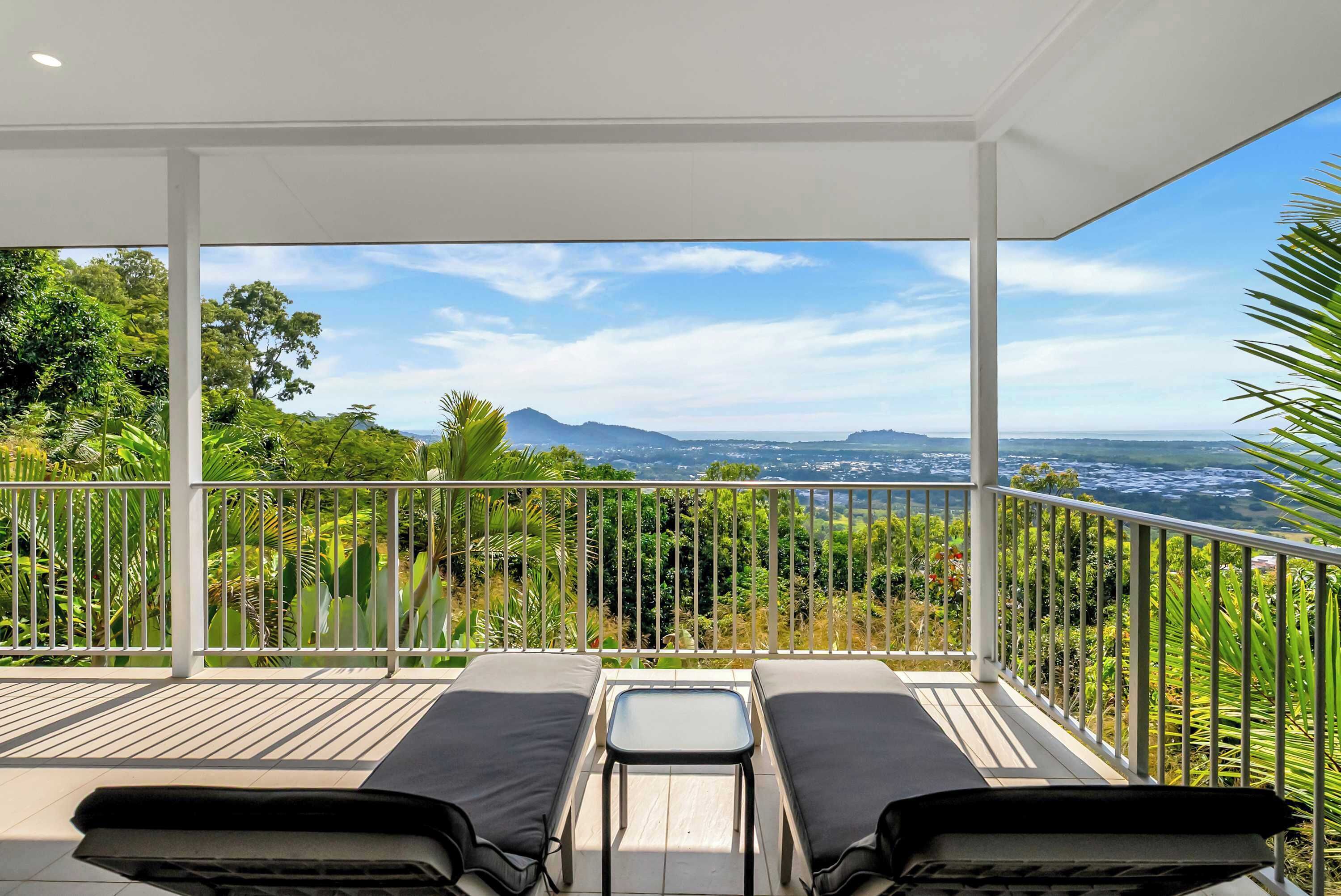Un balcon avec deux fauteuils et une petite table, donnant sur un paysage verdoyant, avec des arbres et des collines à l’horizon.