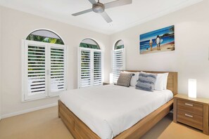 Ein Schlafzimmer mit einem Bett, einem Nachttisch, einem Deckenventilator und einem Bild mit einer Strandansicht.
