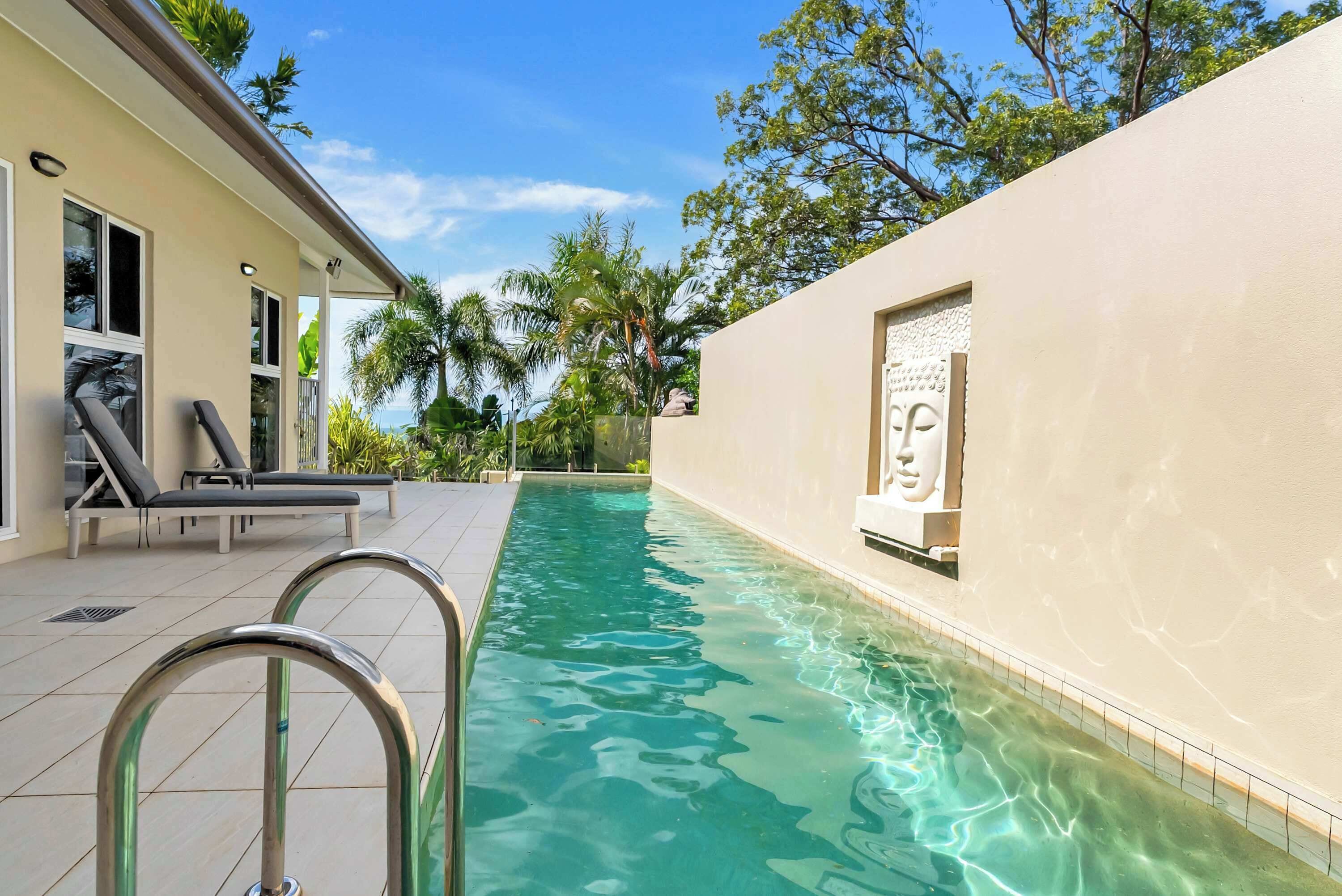 A swimming pool with clear water, surrounded by a building with a white exterior and a door with glass panels.