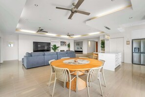 A modern living space with a dining area, sofas, a TV, and ceiling fans. - Tranquillity - Poolside Sanctuary & Rainforest Views (Smithfield)