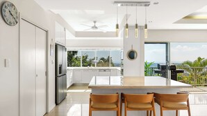 A modern kitchen with a large island, bar stools, and a view of the outdoors. - Tranquillity - Poolside Sanctuary & Rainforest Views (Smithfield)