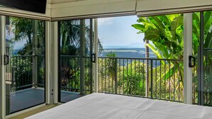 A bedroom with a large sliding glass door leading to a balcony with a view of a tropical landscape. - Tranquillity - Poolside Sanctuary & Rainforest Views (Smithfield)