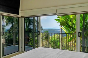 Ein Schlafzimmer mit einer großen Schiebetür, die auf einen Balkon mit Blick auf eine tropische Landschaft führt.