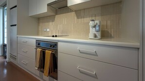 A modern kitchen with white cabinetry, a built-in oven, and a wall-mounted coffee machine. - Silver Sands Beach House (Aldinga Beach)