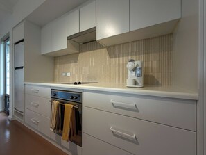 A modern kitchen with white cabinetry, a built-in oven, and a wall-mounted coffee machine. - Silver Sands Beach House (Aldinga Beach)