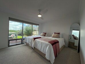 A bedroom with a bed, a ceiling fan, a large window, and a view of the outdoors. - Silver Sands Beach House (Aldinga Beach)