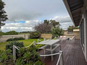 A deck with a barbecue area, outdoor furniture, and a view of the surrounding landscape. - Silver Sands Beach House (Aldinga Beach)