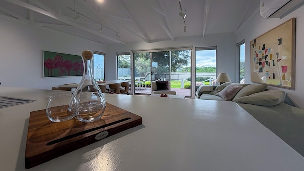 A modern living room with a large white table, a glass decanter, and a wooden tray. - Silver Sands Beach House (Aldinga Beach)